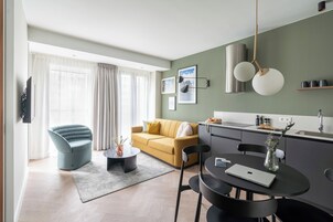 Una sala moderna con un sofá, una mesa de comedor con sillas, un televisor de pantalla plana y una zona de cocina con un fregadero y una encimera.