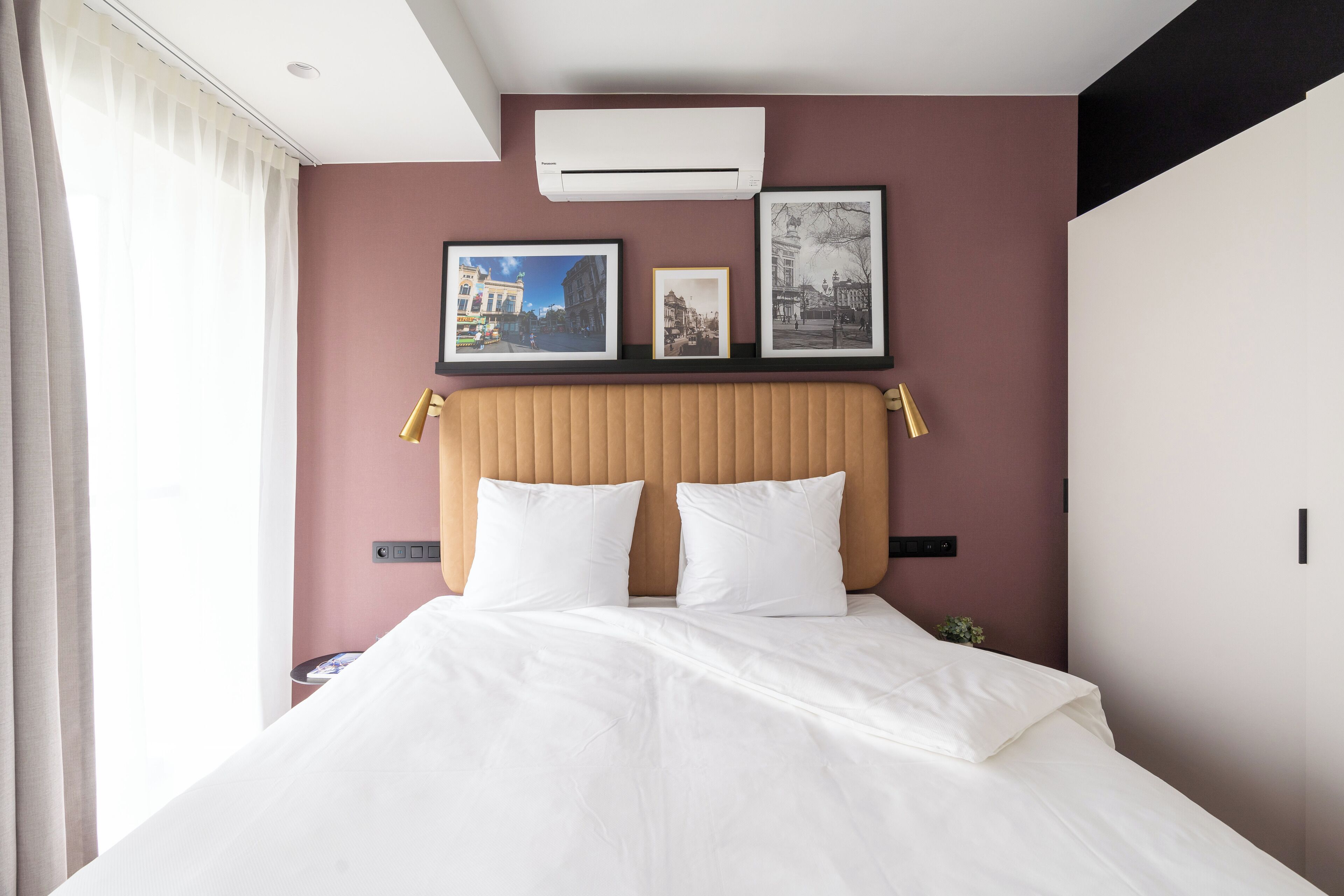 Una habitación de hotel con una cama, cabecera y cuadros en la pared.