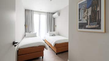 A hotel room with two beds, a window with curtains, an air conditioning unit, and a framed picture on the wall.
