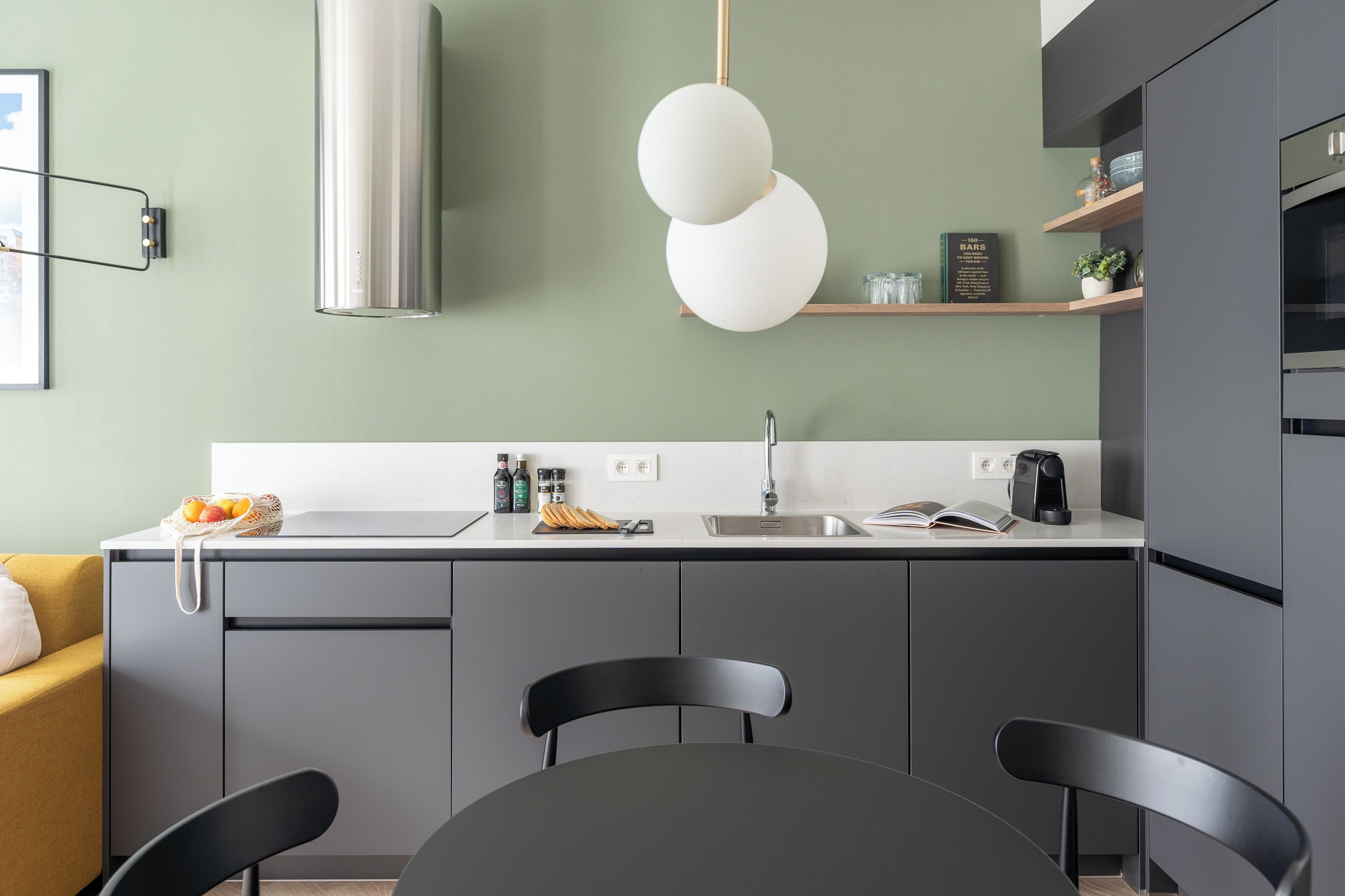 A modern kitchen with grey cabinets, a white countertop, and a hanging spherical light fixture.