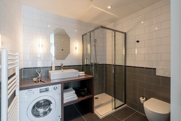 A modern bathroom with a glass-enclosed shower, a washing machine, and a toilet.