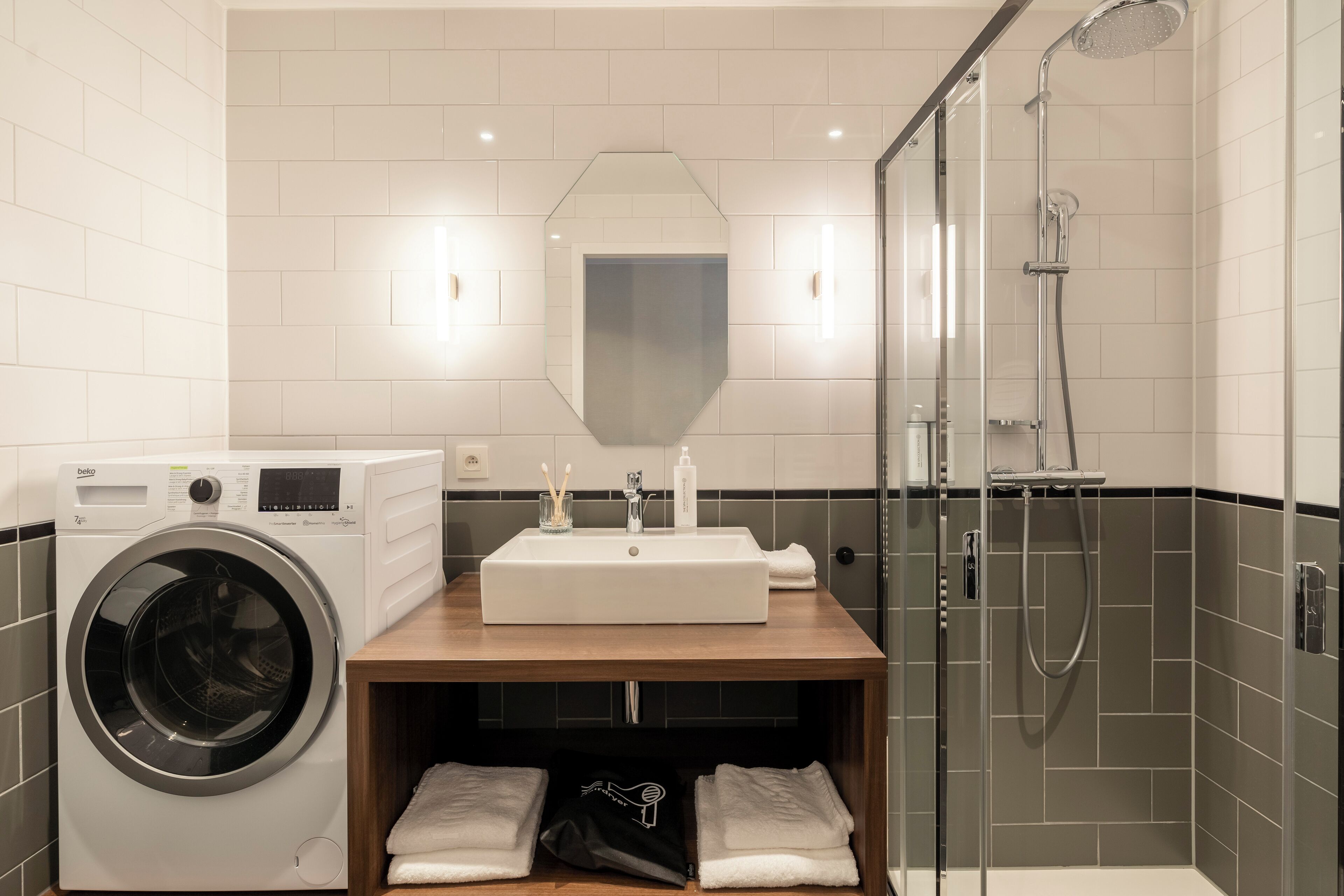 A modern bathroom with a built-in washing machine, a sink with a mirror above, and a glass-enclosed shower area.