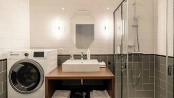 A modern bathroom with a built-in washing machine, a sink with a mirror above, and a glass-enclosed shower area.