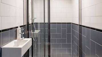 Un baño moderno con ducha envuelta en vidrio, un lavamanos blanco y paredes con azulejos negros.