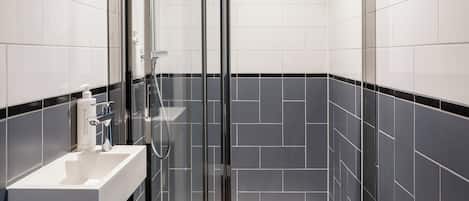 Un baño moderno con ducha envuelta en vidrio, un lavamanos blanco y paredes con azulejos negros.