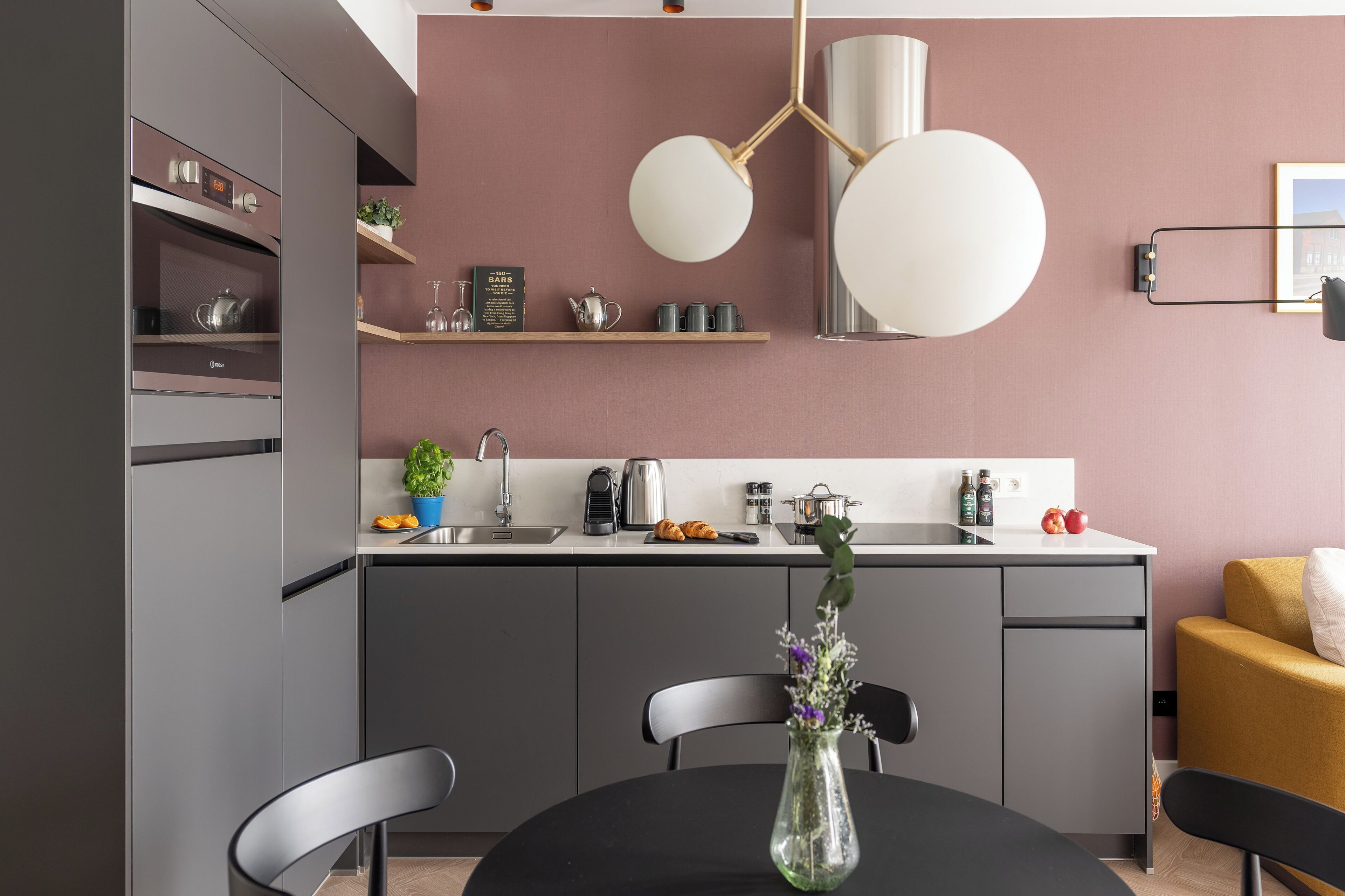 A modern kitchen with grey cabinets, a black dining table, and a vase with flowers.
