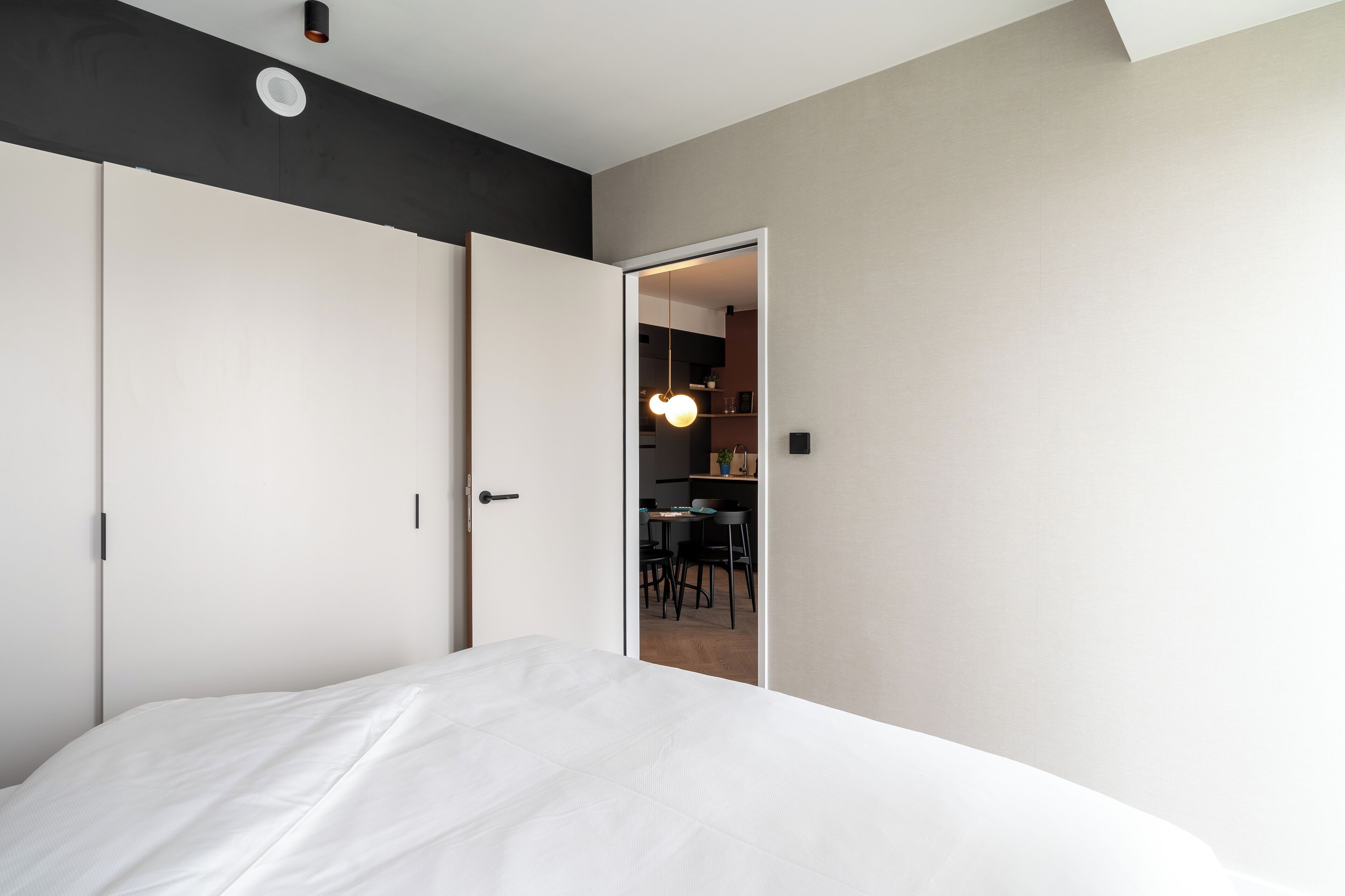A bedroom with a bed, a wardrobe, and a door leading to a dining area.