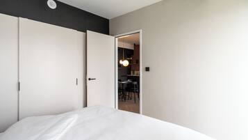 A bedroom with a bed, a wardrobe, and a door leading to a dining area.