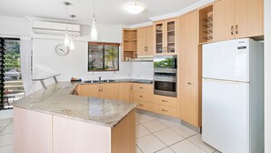 Une cuisine moderne avec des meubles en bois, un four encastré, un réfrigérateur et un grand îlot central doté d’un plan de travail en granit.