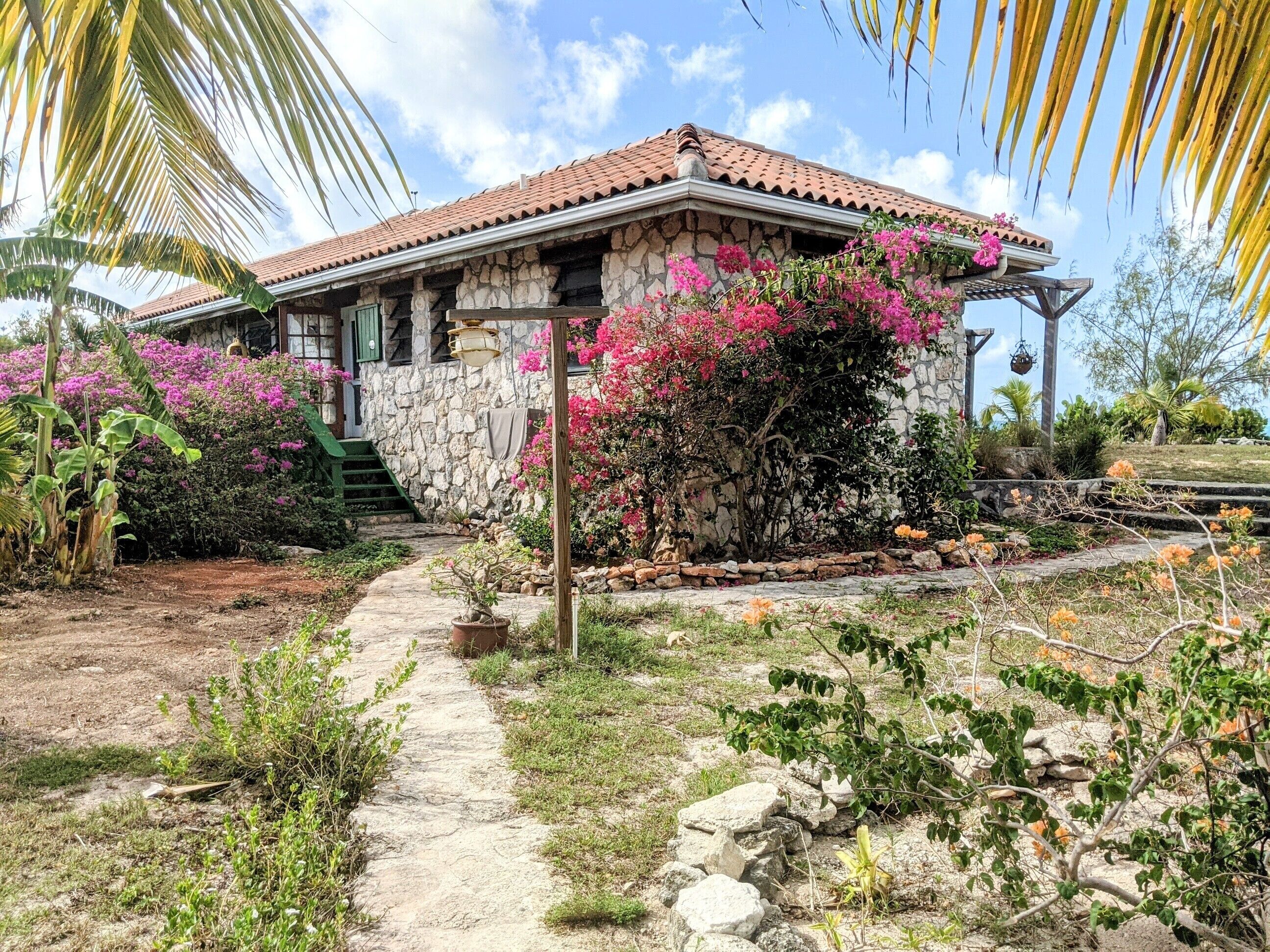 Ein Haus aus Stein mit Ziegeldach, umgeben von einem Garten mit rosa Bougainvillea und anderen Pflanzen.