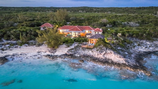 Il s’agit d’une propriété située en bord de mer, comprenant plusieurs bâtiments, dont une maison principale avec un toit rouge et une dépendance plus petite recouverte d’un toit de chaume.