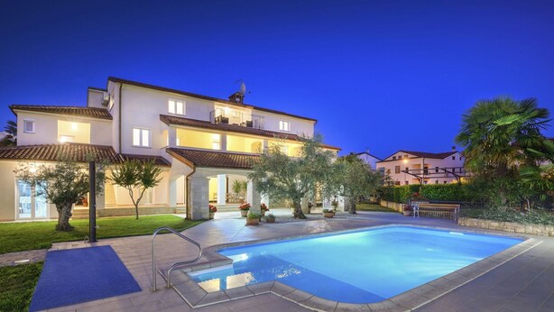 Une maison à deux étages avec une piscine, entourée de verdure et dotée d’une pelouse bien entretenue.