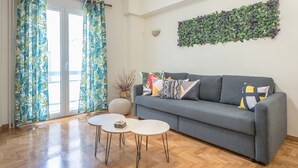 Ett vardagsrum med en grå soffa, två vita soffbord och tropiska gardiner.
