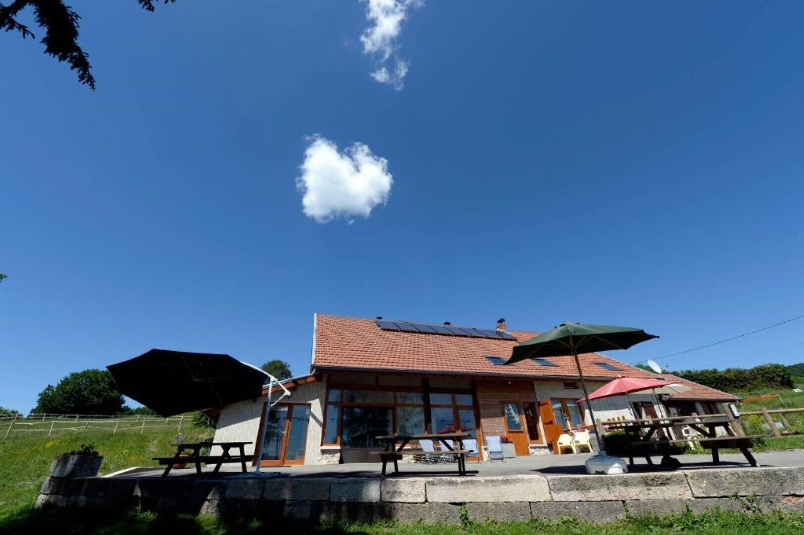 Un bâtiment dot é d’un toit en tuiles, de grandes fenêtres et d’un espace extérieur aménagé avec des parasols.