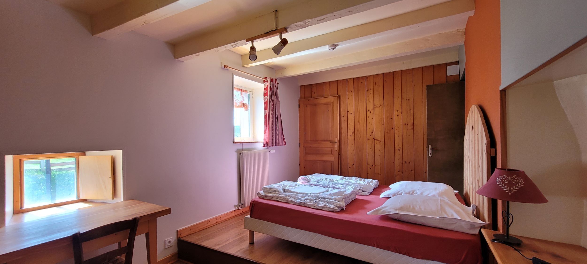 A bedroom with a bed, a window, a desk, and a radiator.