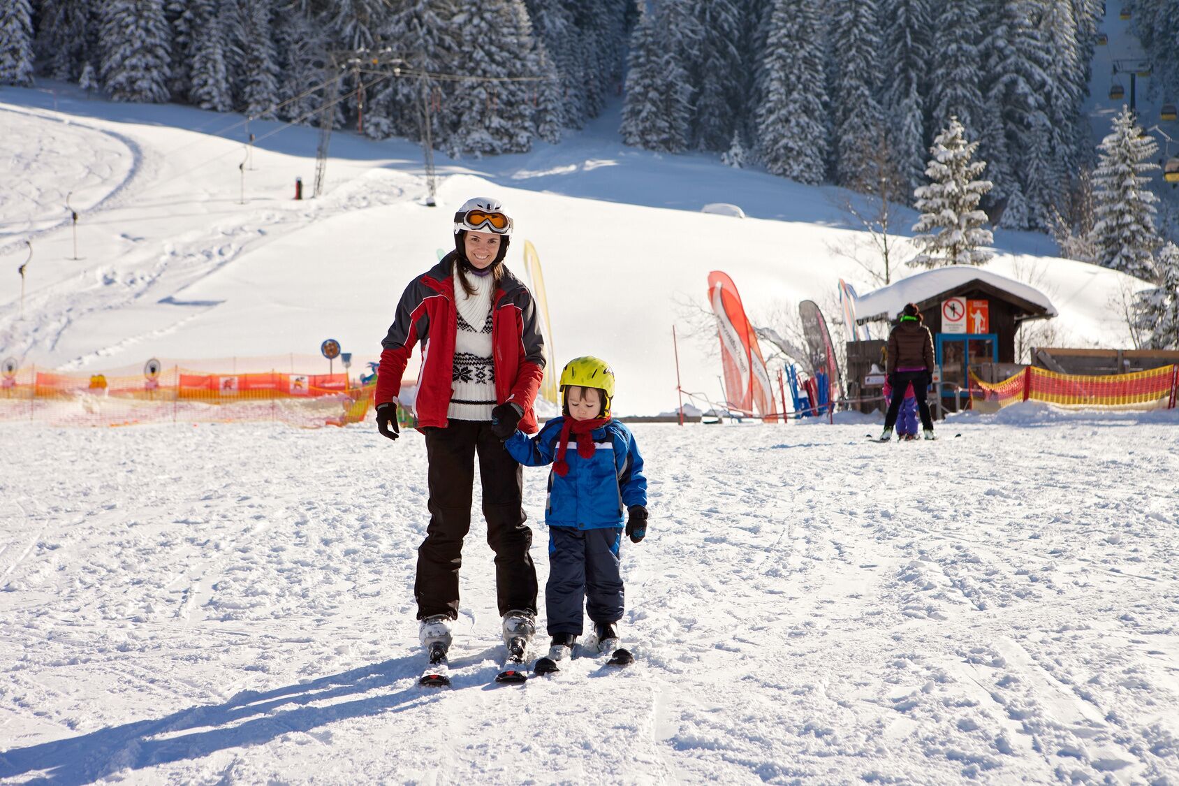 Pista de esquí nevada con una persona y un niño con equipo de esquí.