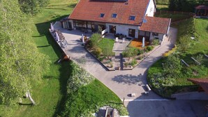 Une maison avec un toit recouvert de tuiles rouges, des panneaux solaires, un patio couvert et un jardin.