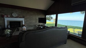 A living room with a fireplace, a large bed, a television, and a view of the sea. - Lake views and Sunsets for Days (Lorain)