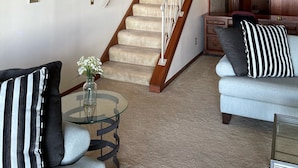 A living room with a staircase, a glass coffee table, two sofas, and decorative wall art. - Lake views and Sunsets for Days (Lorain)