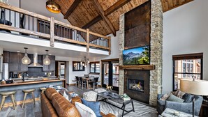 A spacious living area with a high ceiling, a stone fireplace, and a large window overlooking a mountainous landscape. - Slice of Heaven just steps from Lake Estes! Indoor/Outdoor Fireplace and Jacuzzi (Estes Park)