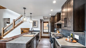 A modern kitchen with a central island, wooden staircase, and pendant lighting. - Slice of Heaven just steps from Lake Estes! Indoor/Outdoor Fireplace and Jacuzzi (Estes Park)