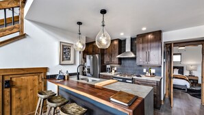 A modern kitchen with a central island, bar stools, stainless steel appliances, and pendant lighting. - Slice of Heaven just steps from Lake Estes! Indoor/Outdoor Fireplace and Jacuzzi (Estes Park)