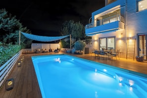 Une piscine avec une terrasse en bois, du mobilier d’extérieur et un bâtiment à deux étages doté de balcons.