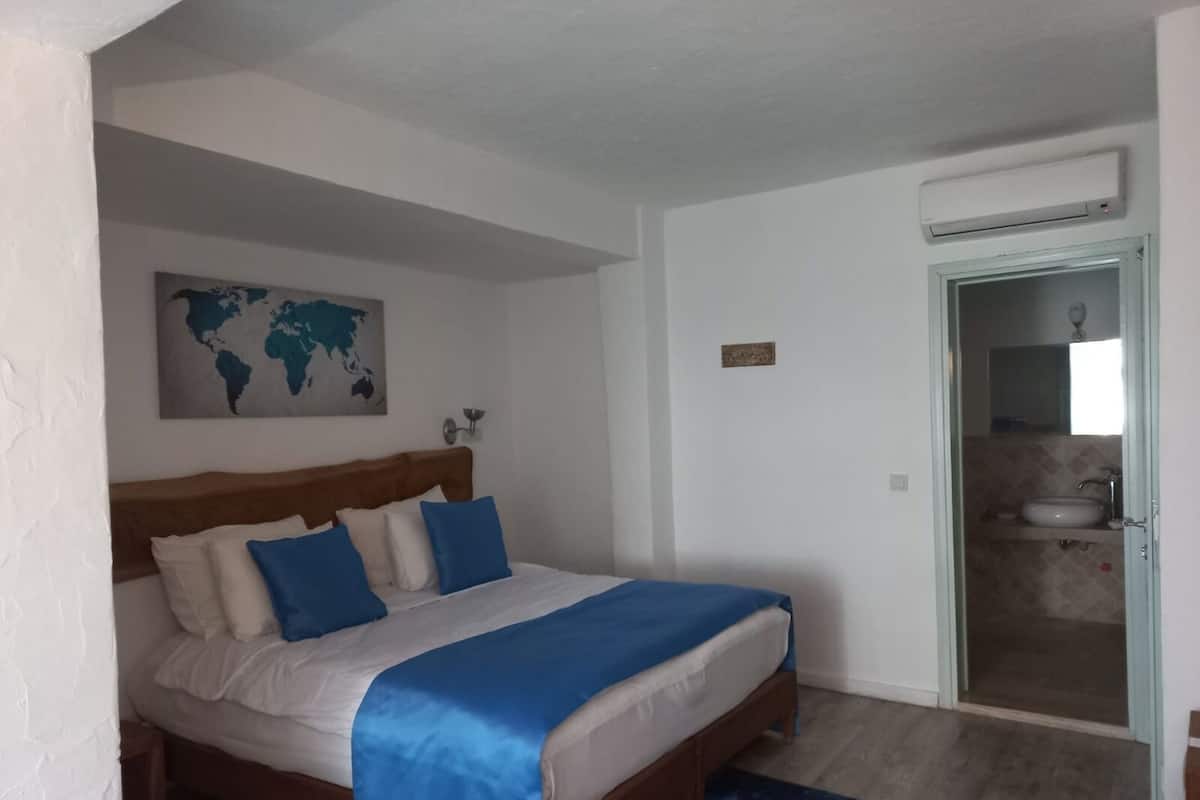A bedroom with a bed, a world map on the wall, and a bathroom visible through an open door.