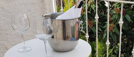 A small round table with two wine glasses and a metal bucket on a balcony.