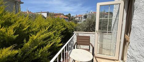 Un balcón con mesa y sillas, una puerta y vistas del barrio.