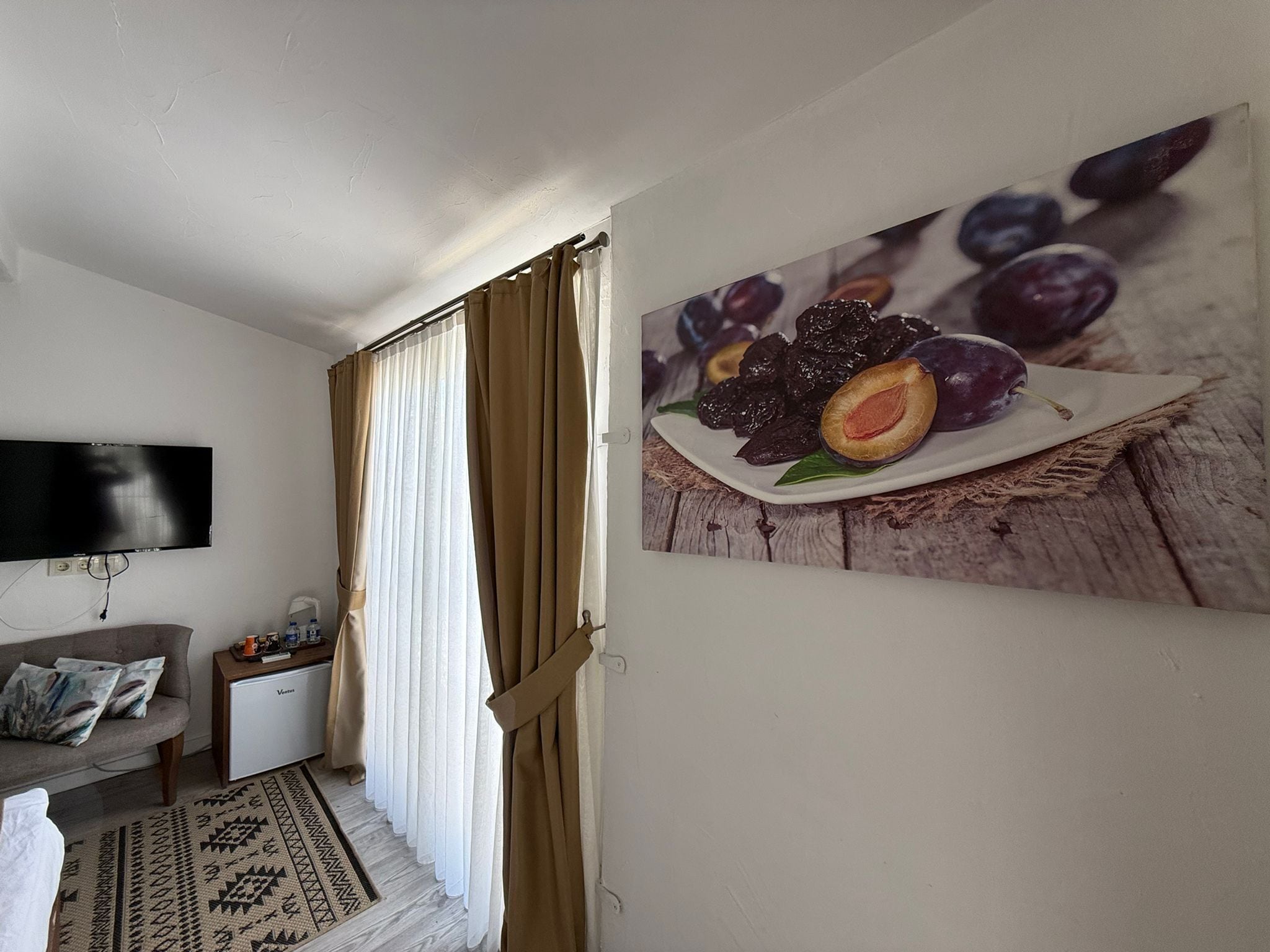 Una sala de estar con un televisor de pantalla plana, un sofá, una mesita y un cuadro de ciruelas colgado en la pared.