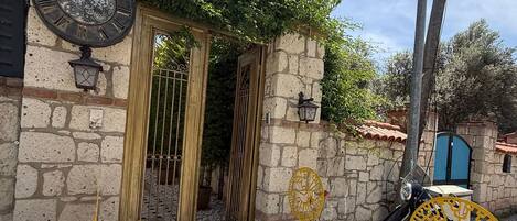 A stone wall with a gate, a clock, and a scooter parked outside.