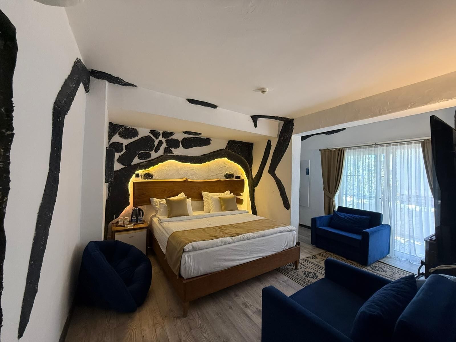 A bedroom with a large bed, a nightstand, a blue sofa, and a window with curtains.