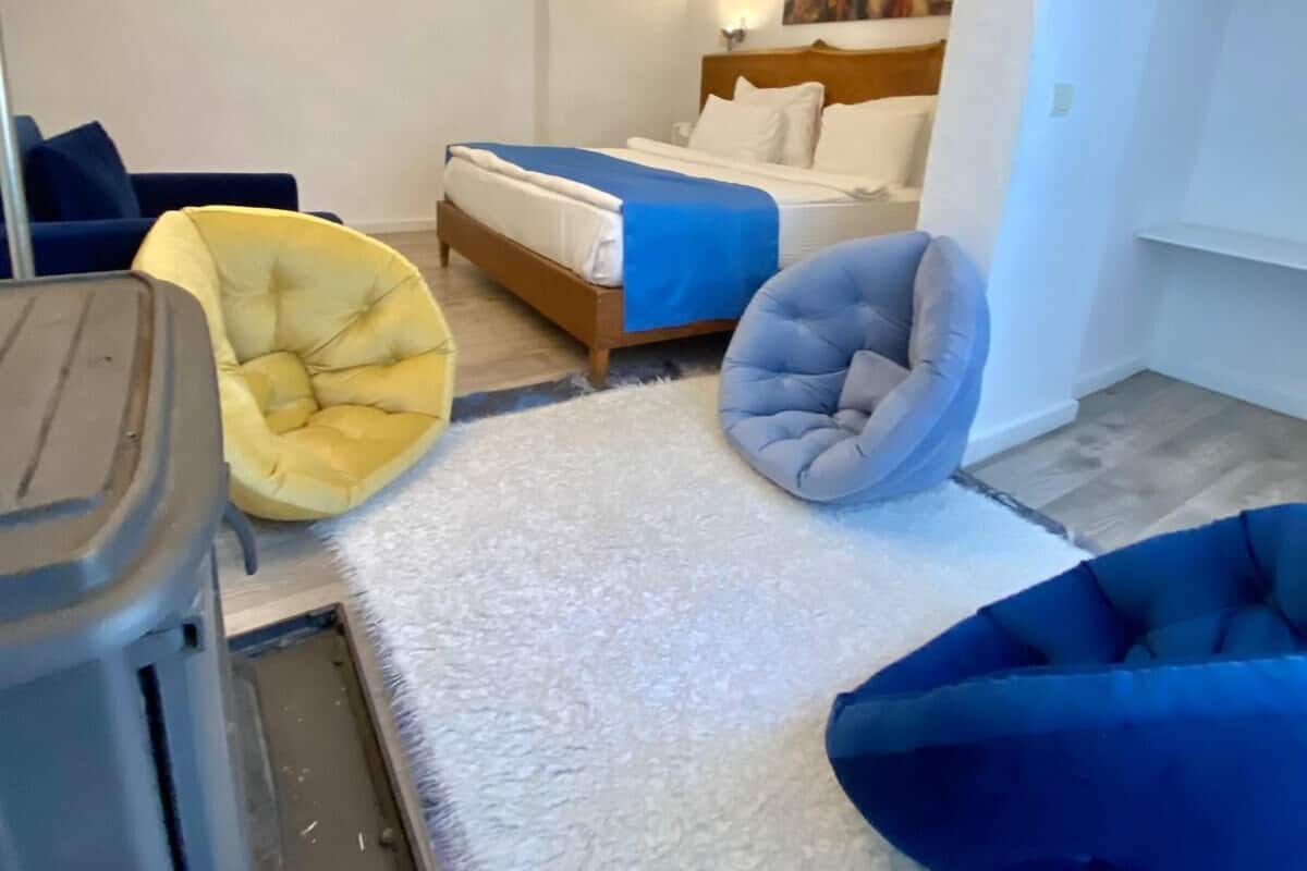 A hotel room with a bed, a sofa, a chair, and a trash bin.