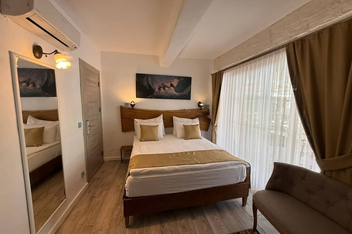 A hotel room with a bed, a chair, a painting on the wall, and a window with curtains.