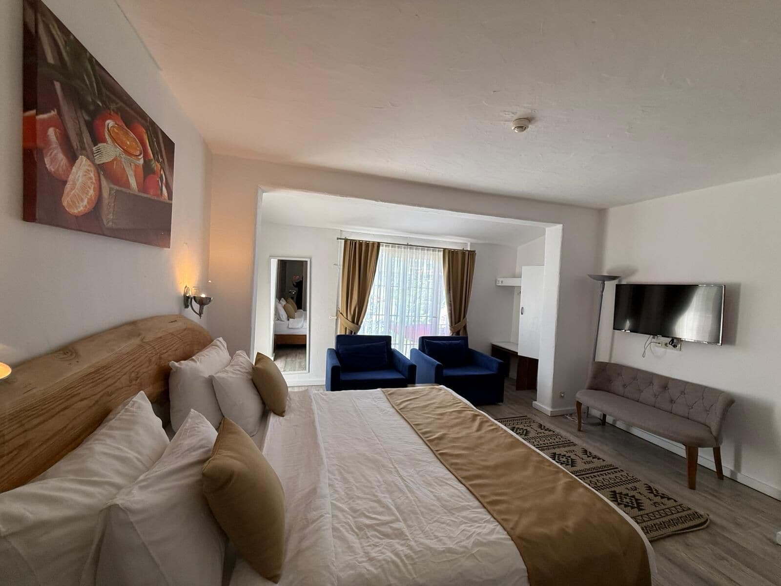 A hotel room with a large bed, a TV, a sofa, and a desk.