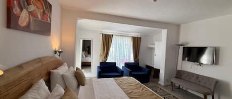 A hotel room with a large bed, a TV, a sofa, and a desk.