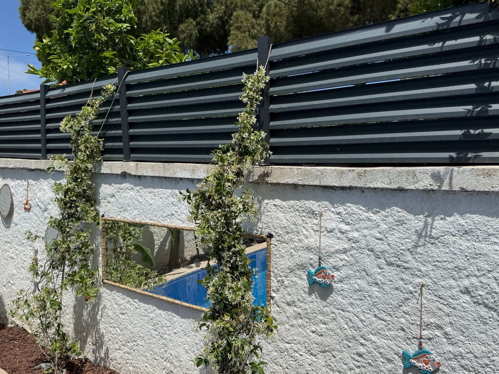 A white textured wall with a black metal structure, a small blue window, and decorative fish ornaments.
