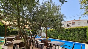 An outdoor pool area with wooden deck seating and a clear blue pool. - Alaçatı Otel Rebetiko (Cesme)