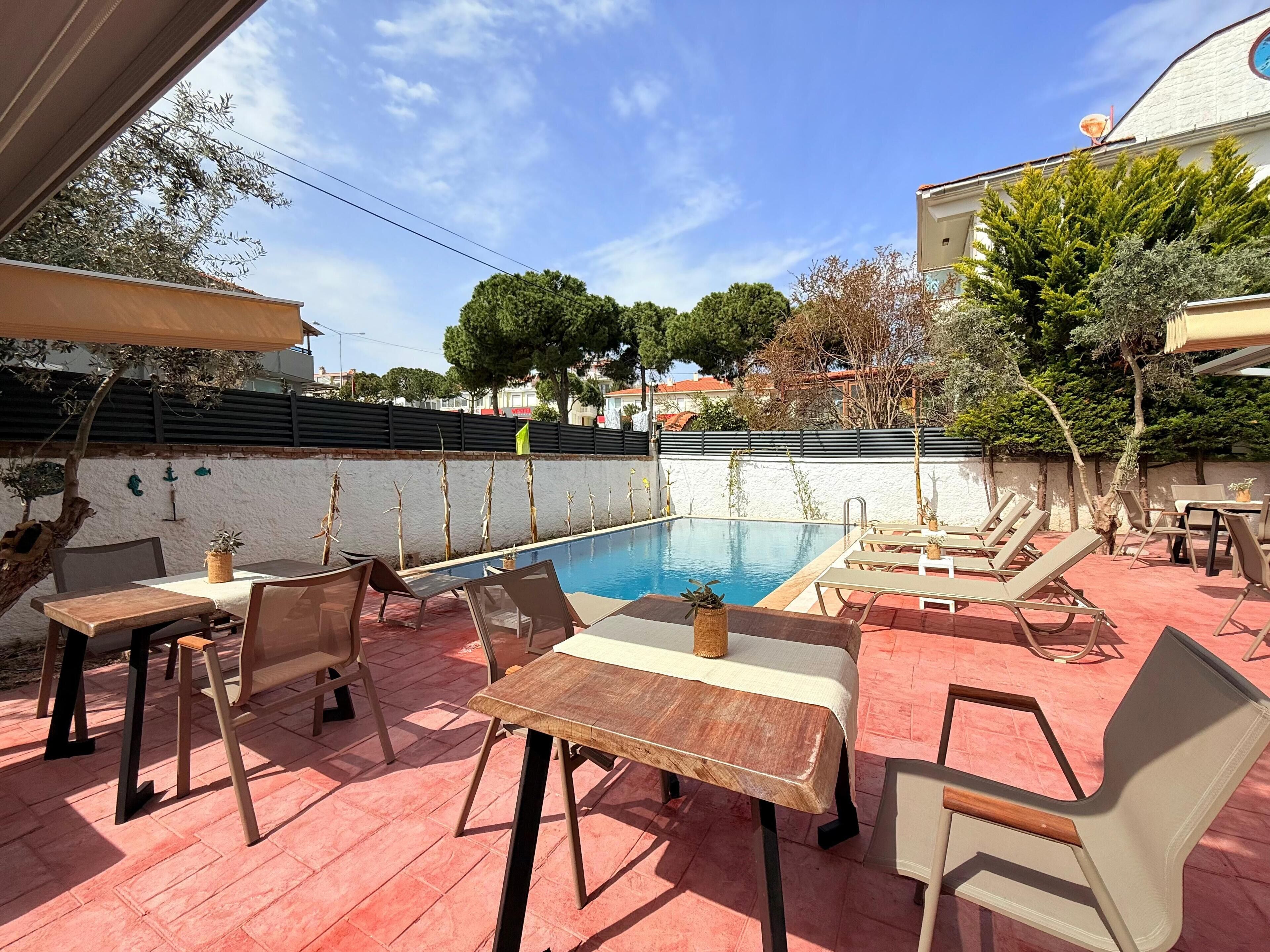 Zona junto a la piscina con sillas de descanso y mesas, una piscina y vistas de los alrededores.
