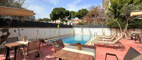 Zona junto a la piscina con sillas de descanso y mesas, una piscina y vistas de los alrededores.