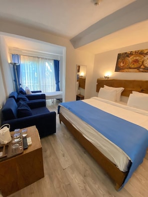 A hotel room with a large bed, a sofa, a small table with toiletries, a window with curtains, and a wall clock. - Alaçatı Otel Rebetiko (Cesme)