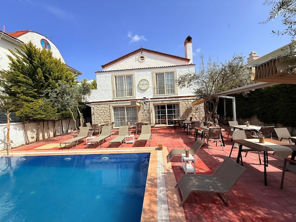 A two-story house with a pool, outdoor seating, and a stone wall. - Alaçatı Otel Rebetiko (Cesme)