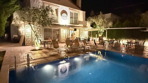 A nighttime view of a swimming pool area with lounge chairs and a stone building with a sign. - Alaçatı Otel Rebetiko (Cesme)