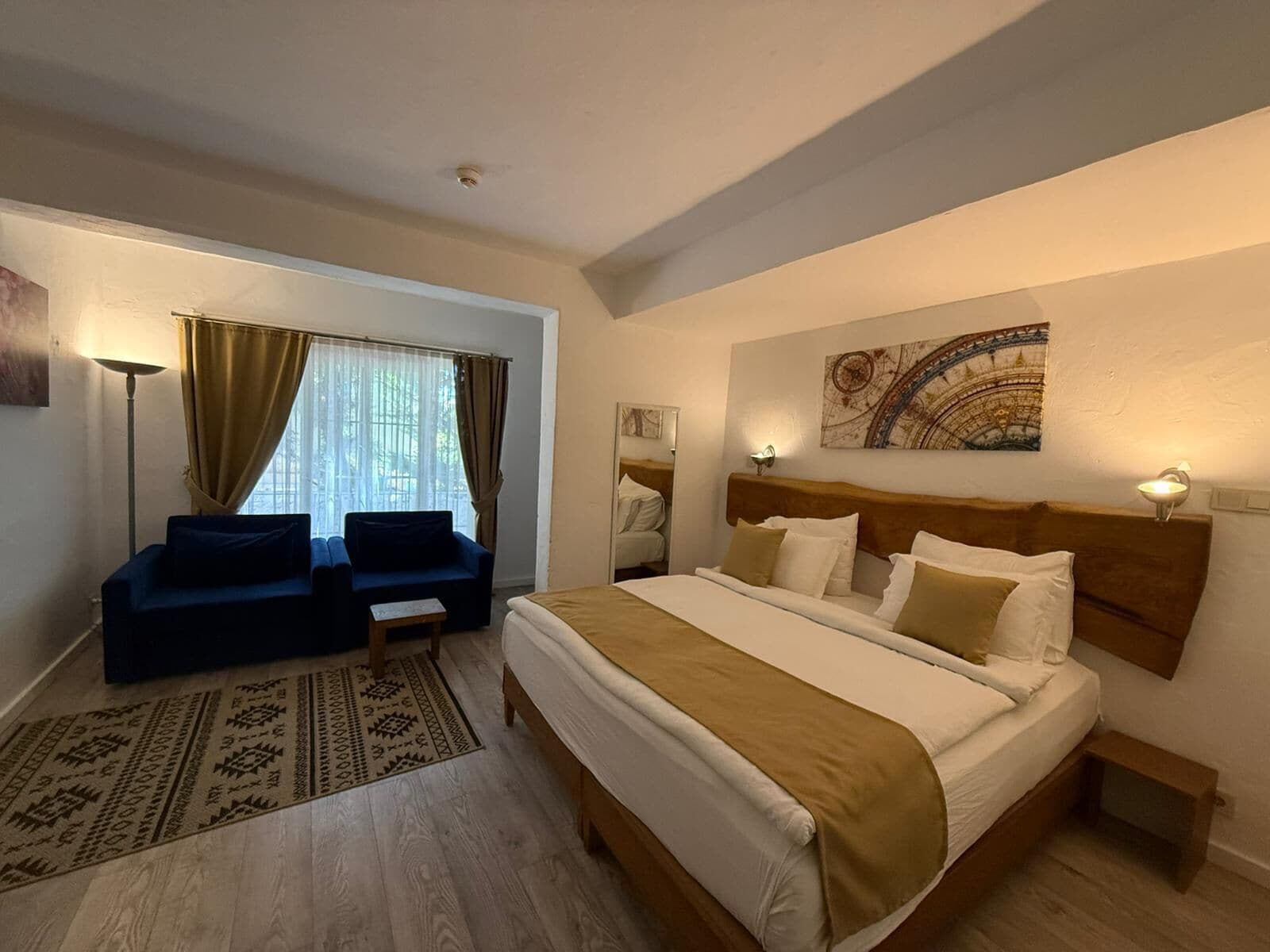 Habitación de hotel con cama, dos sillones, una mesita, una lámpara de pie y una ventana con cortinas.