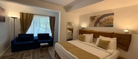 Habitación de hotel con cama, dos sillones, una mesita, una lámpara de pie y una ventana con cortinas.