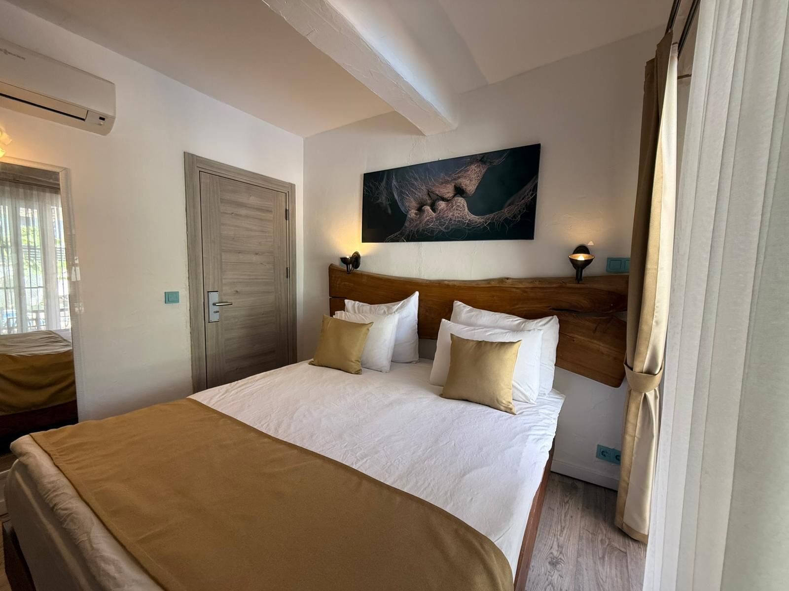Ett hotellrum med en säng, en träpanel som huvudgavel, en tavla på väggen och ett fönster med gardiner.