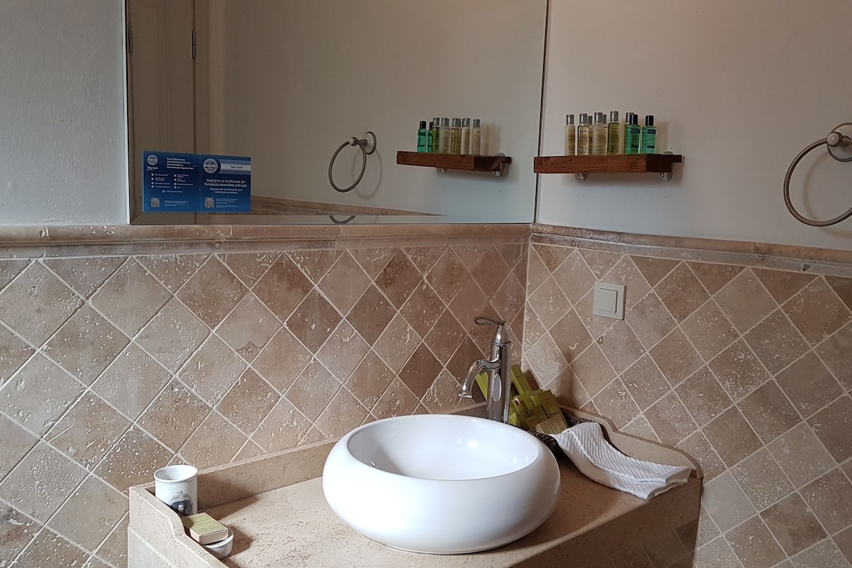 A bathroom with a white sink, a mirror, and a shelf with toiletries.
