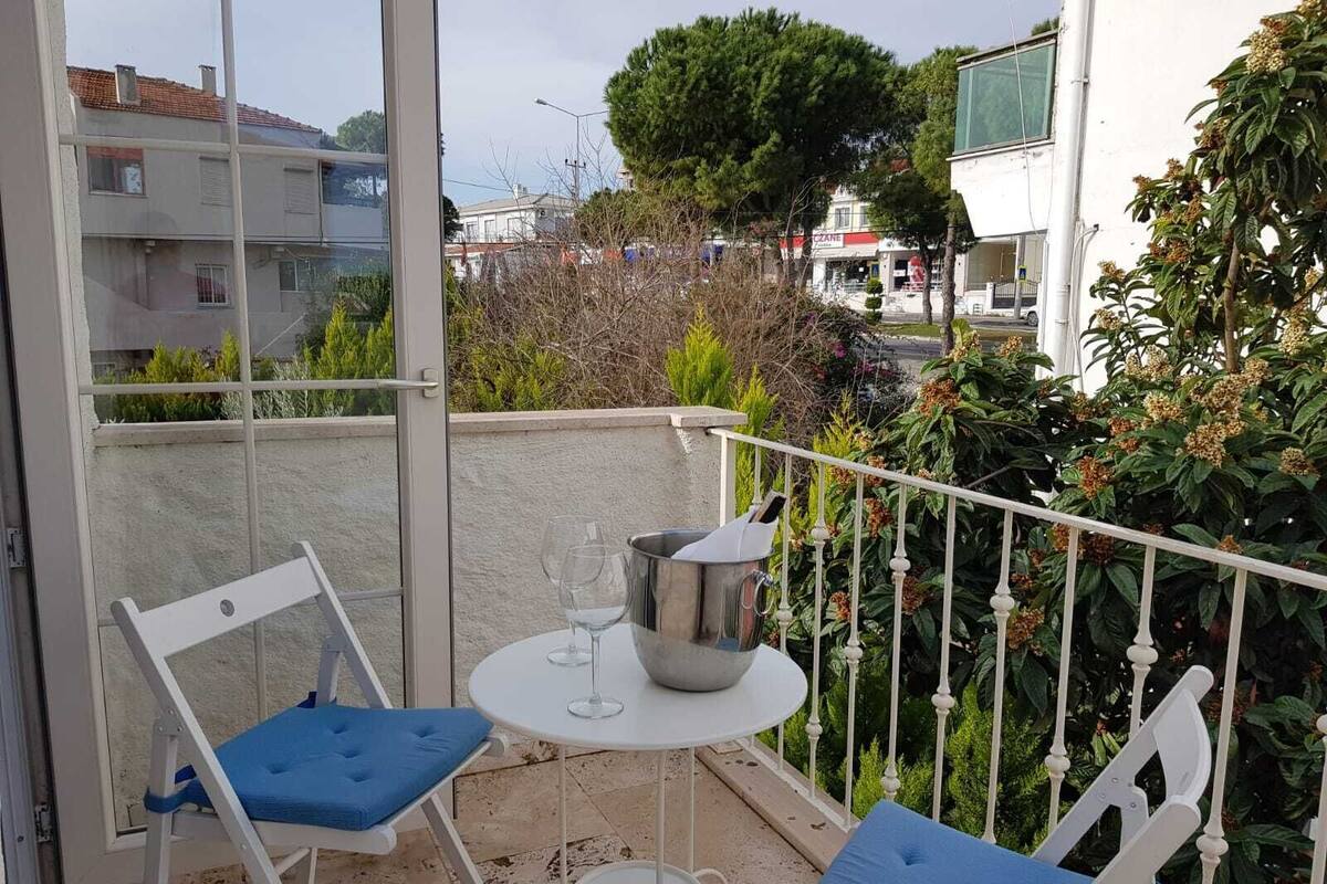 A balcony with two white chairs and a small table, a metal bucket, and a wine glass.
