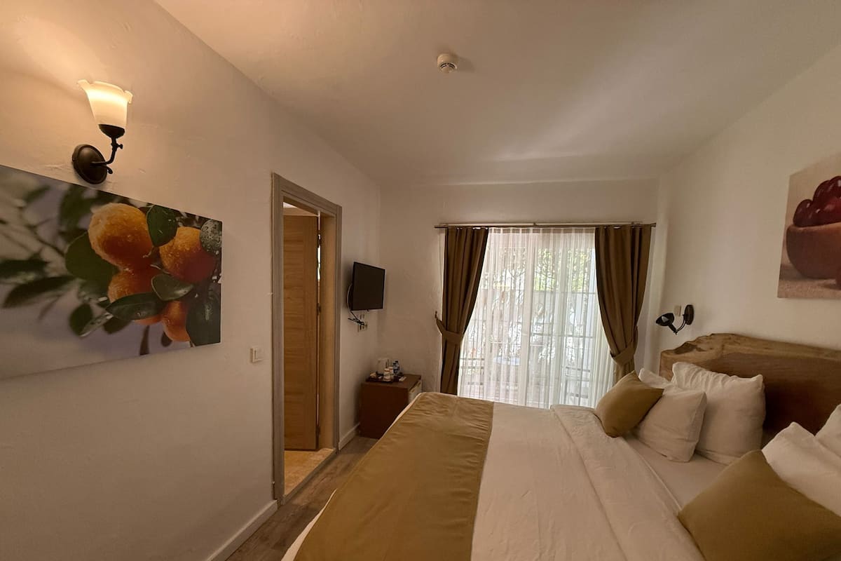 A hotel room with a bed, a TV, a painting, and a window with curtains.